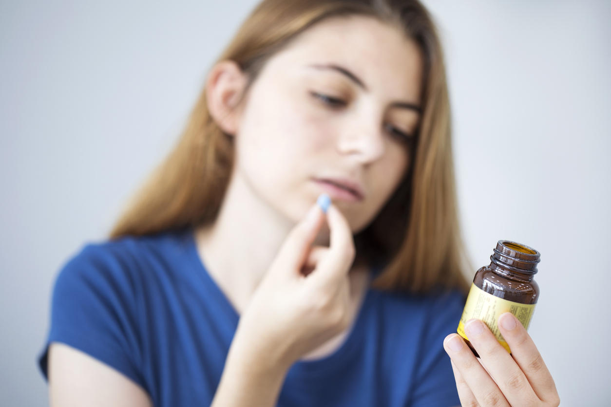 young woman taking a pill while reading the bottle