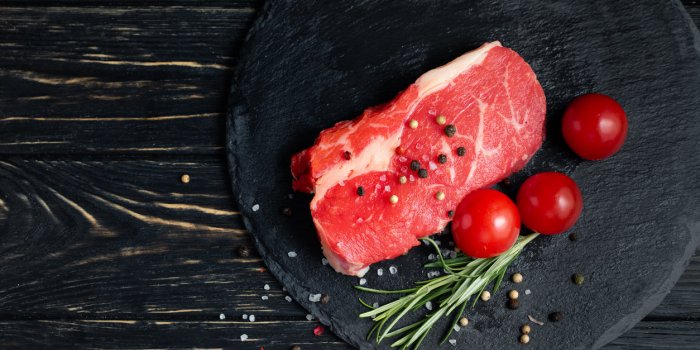 one pieces of juicy raw beef with rosemary on a stone cutting board on a black wooden table background meat for barbecue ...