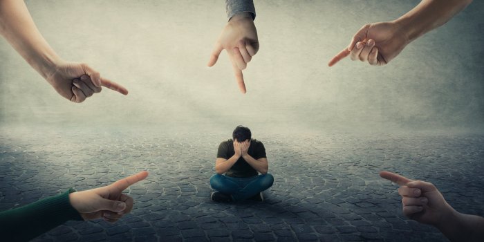 stressed man, under pressure, sitting on floor cover face feel discomfort as a lot of hands pointing forefingers to him b...