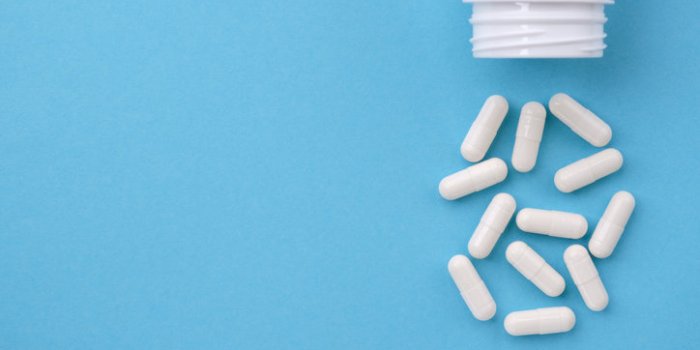 white capsules falling from the white bottle on blue paper background concept of pharmacy
