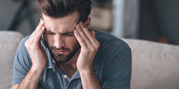 feeling stressed frustrated handsome young man touching his head and keeping eyes closed while sitting on the couch at home