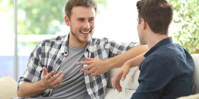 two friends talking sitting in a couch in the living room with a window in the background at home
