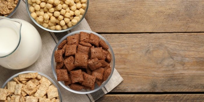 different breakfast cereals and milk on wooden table, flat lay space for text