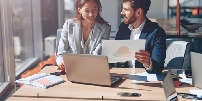 two smiling business people during work meeting in modern office explaining statistics data to each other looking at docu...