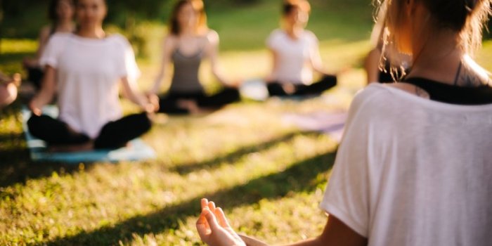 group of young sporty woman practicing yoga lesson with instructor, sitting in lotus pose focus of camera at teacher rear...