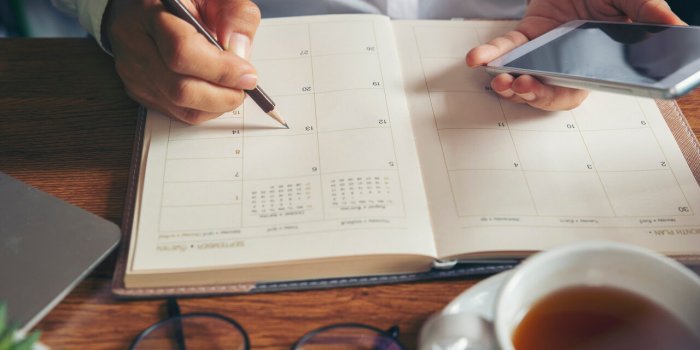 on 2020 calendar book,female'hand of planner writing daily appointmentwoman mark and noted schedule(holiday trip) on diar...