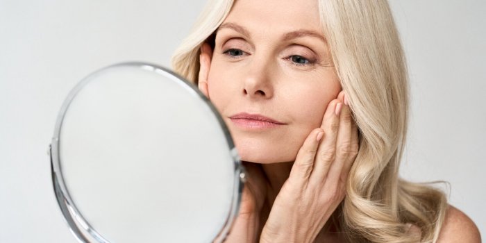 closeup portrait of gorgeous happy middle age woman looking at mirror touching her skin enjoying treatment for dry skin a...