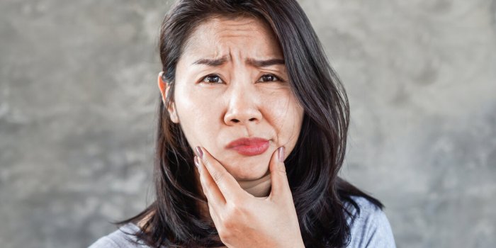 depressed asian woman having problem with bell's palsy facial palsy, hand holding her face