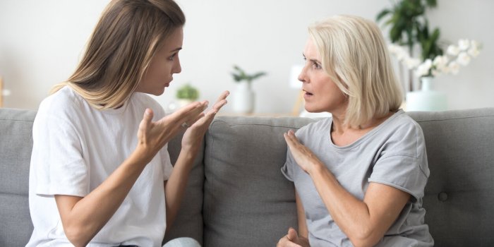 angry young woman has disagreement with annoyed old mother in law, grown daughter arguing fighting quarreling with senior...