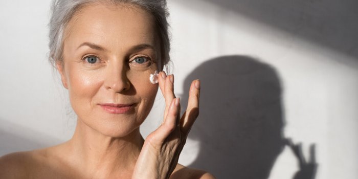 face skin care woman applying cosmetic cream on clean hydrated skin portrait smiling caucasian senior female model with n...