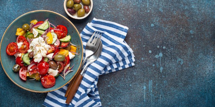 greek fresh healthy colorful salad with feta cheese, vegetables, olives in blue ceramic bowl on rustic concrete backgroun...