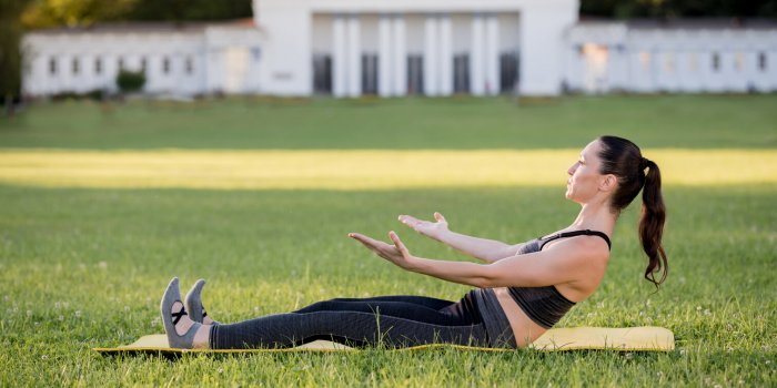 beautiful young woman lying on a yellow mattress, pose while wearing a tight sports outfit in the park doing pilates or y...