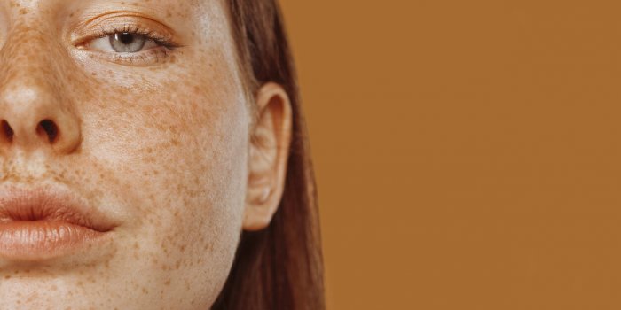 close-up portrait of half face red-haired girl with freckle and blue eye beautiful young woman's face shot female model w...