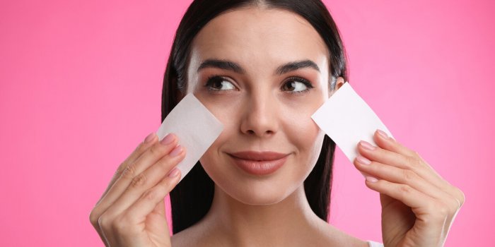 beautiful woman using mattifying wipes on pink background