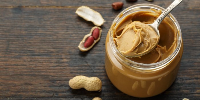 peanut paste in an open jar and peanuts in the peel scattered on the table