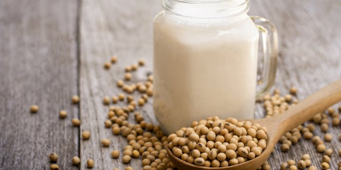 soy bean in wooden spoon and soy milk in glass jar isolated on wood table background