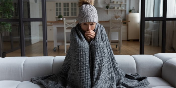 frozen sad latina female sit on couch at freezing cooled studio flat in warm cap and blanket shiver tremble with cold unh...