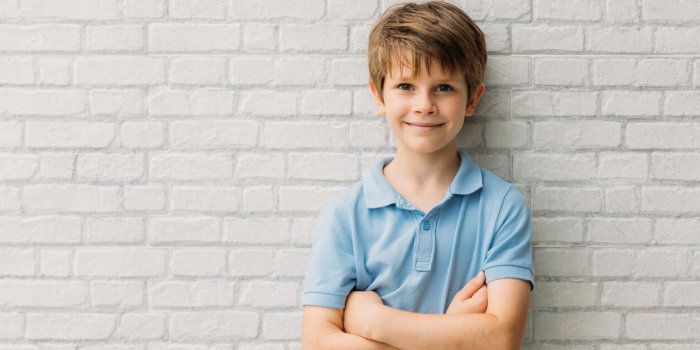 portrait of happy young caucasian boy in casual outfit with arms crossed isolated over white bricks background smiling an...