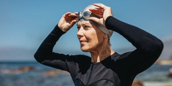 close up of a woman in swim wear standing near the sea female swimmer standing on the beach holding her swimming goggles ...