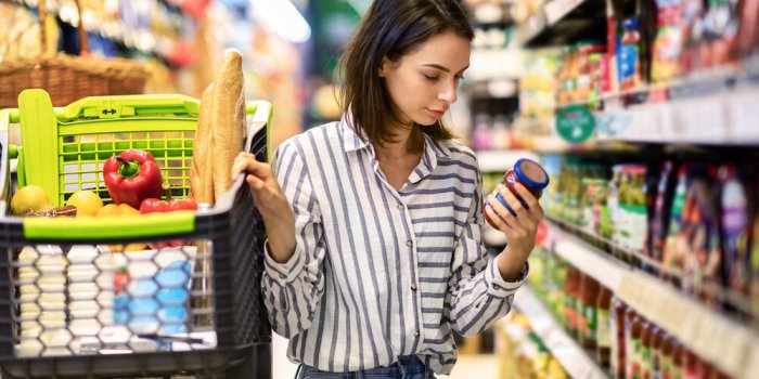 consumption and consumerism portrait of young woman with shopping cart in market buying groceries food taking products fr...
