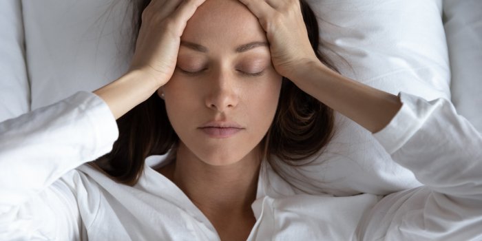 top view close up depressed woman suffering from headache or migraine, touching forehead with hands, lying in bed with cl...