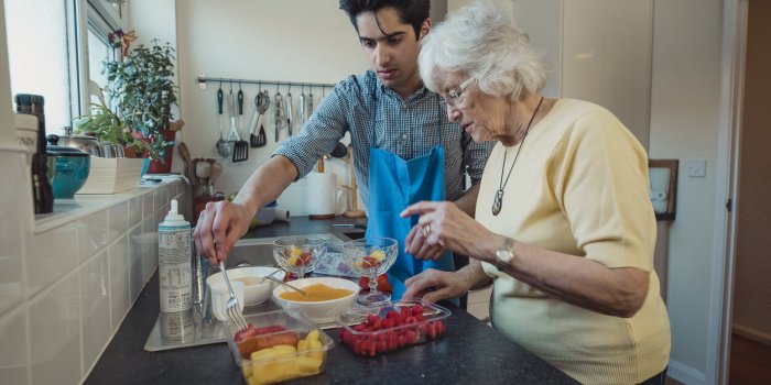 teenage boy making fruit compote with his grandmother in the kitchen of her home