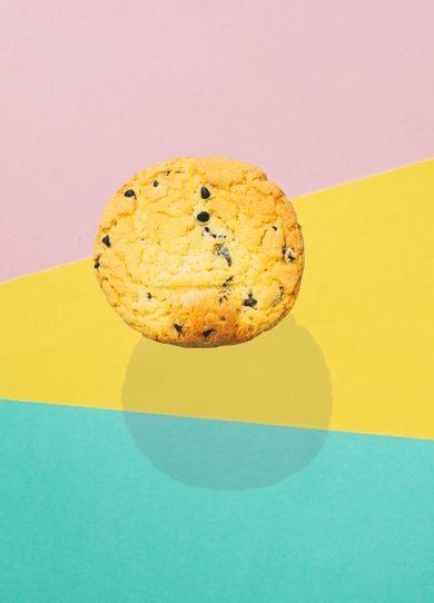 a large round chocolate chip cookie flies in the air with a strong shadow