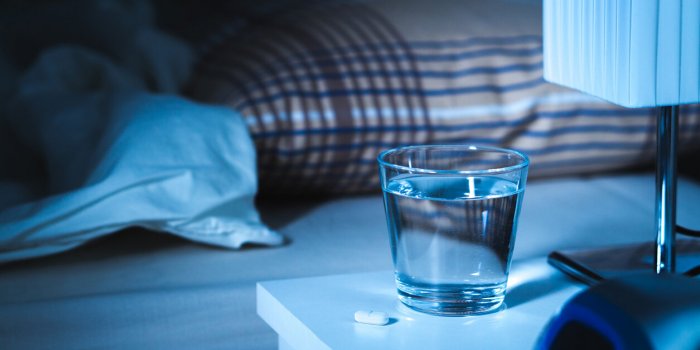 sleeping pill on nightstand next to a glass of water white tablet on table and bed in bedroom insomnia medicine concept