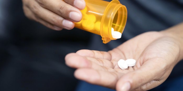 woman hand with pills on, spilling pills out of bottle on dark background