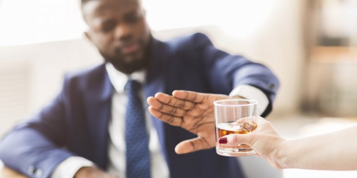 african american businessman saying no to glass of whiskey offered by female colleague, selective focus, copy space