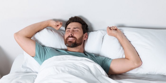 happy man stretching on comfortable pillows in bed at home