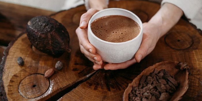 hot handmade ceremonial cacao in white cup woman hands holding craft cocoa, top view on wooden table organic healthy choc...
