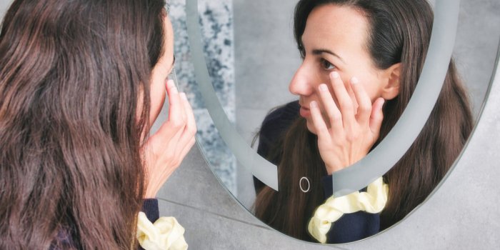 an attractive white caucasian young woman looking in the bathroom mirror touching her wrinkles around her eyes