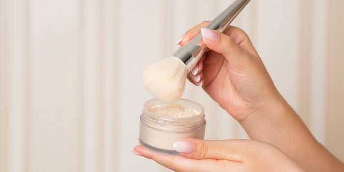 woman with a brush using loose powder on a beige background empty space