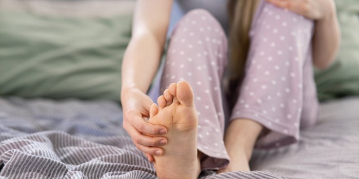 foot pain, woman sitting on bed feeling pain in her foot at home, female suffering from feet ache use hand massage relax ...