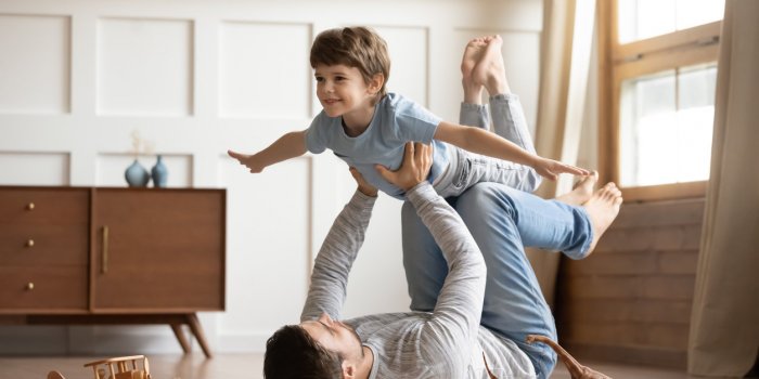 joyful young man father lying on carpet floor, lifting excited happy little child son at home full length carefree two ge...