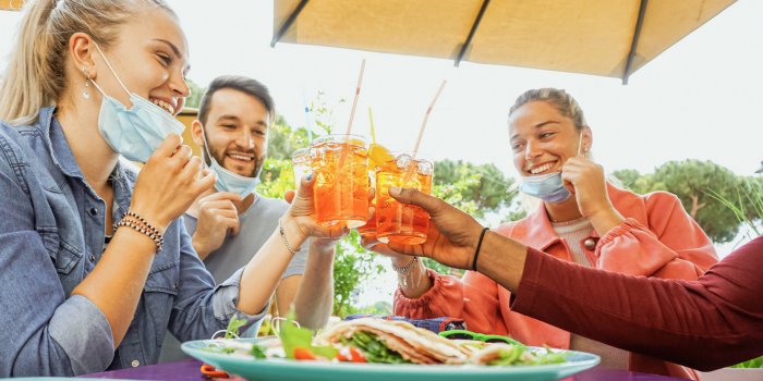 friends drinking coktail and eating snack tapas in a restaurant bar outside in summer days with face mask on to be protec...