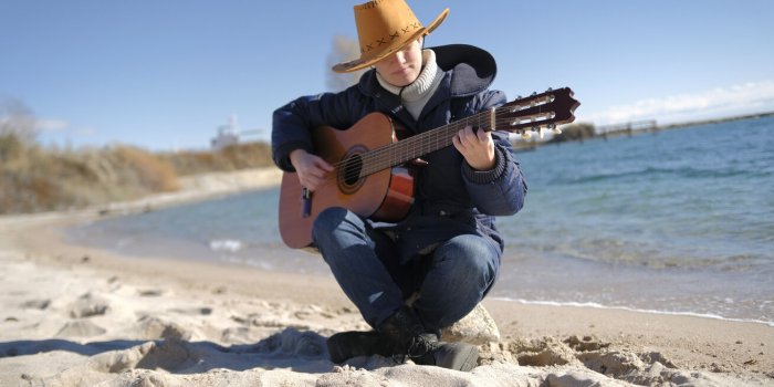 guitar lessons a young mysterious woman in a cowboy hat is playing guitar on the beach by the ocean the scene is calm and...