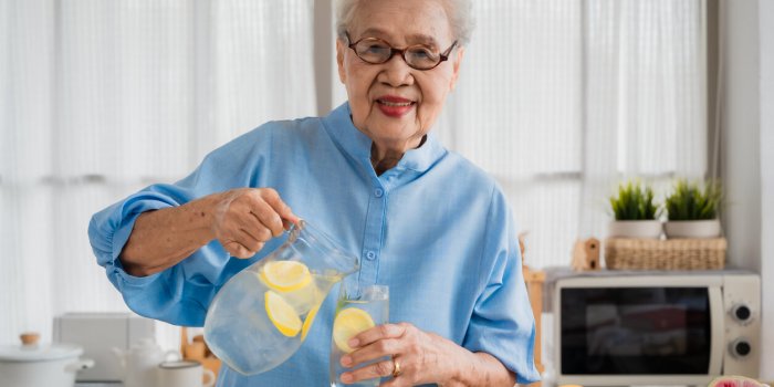 portrait of happy asian senior old elderly woman with gray hair wearing glasses standing smiling and pouring iced lemonad...