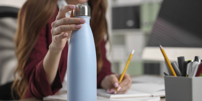 woman holding thermos bottle at workplace, closeup