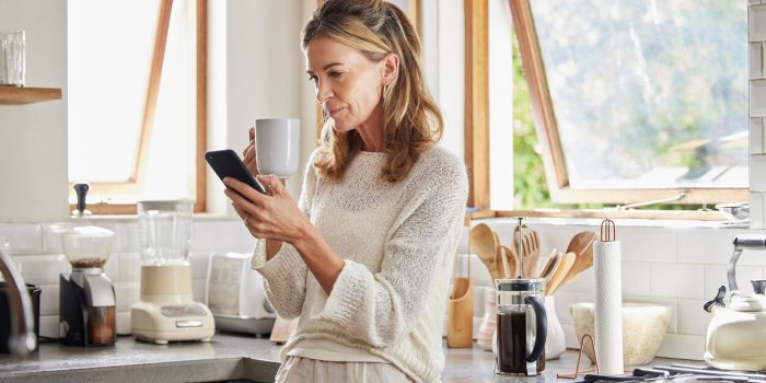 coffee, phone and senior woman in kitchen browsing social media, text message or online app at home relax, tea and readin...