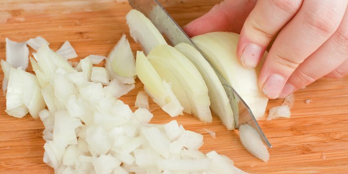 the hands cutting onions on a chopping board