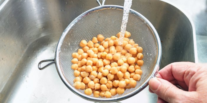 pre-cooked canned chickpeas are rinsed with water in a sieve over the sink before being used in various dishes, healthy l...