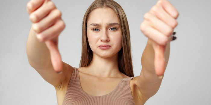 young woman in casual attire giving thumbs down gesture on gray background close up