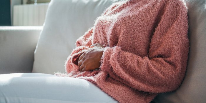 woman in painful expression holding hands against belly suffering menstrual period pain, lying sad on home bed, having tu...
