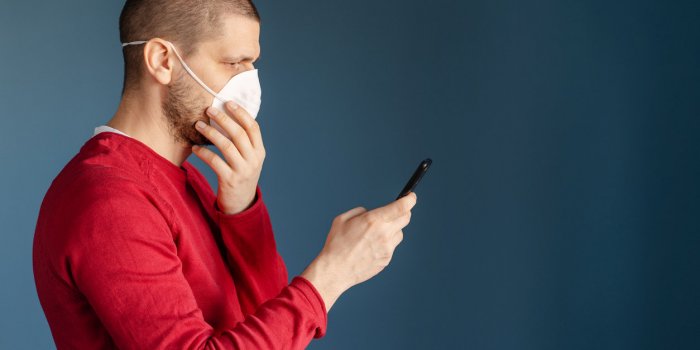 caucasian man wearing red sweater standing in front of the blue background wall using smart phone mobile to send messages...