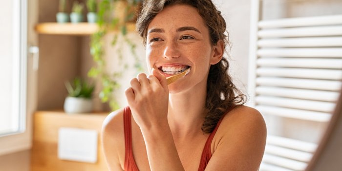 smiling young woman brushing teeth in bathroom portrait of happy girl looking in mirror while using ecological toothbrush...