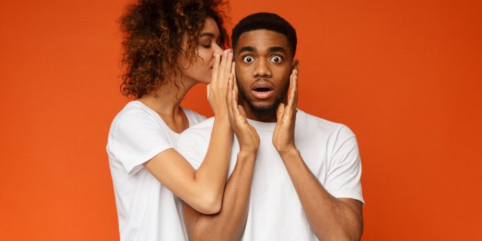 hidden desires black woman whispering her dreams to shocked boyfriend, orange studio background