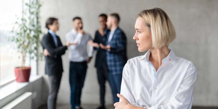 male coworkers whispering behind back of unhappy businesswoman spreading rumors and gossips standing in modern office sex...