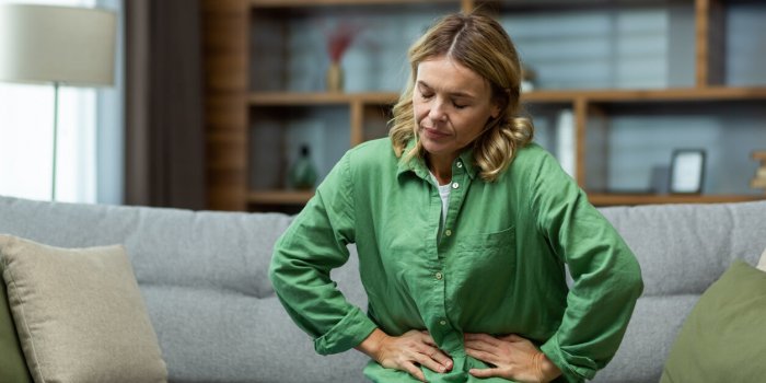 an elderly woman is sitting on the sofa at home, holding her stomach with her hands feels the pain of internal organs, in...